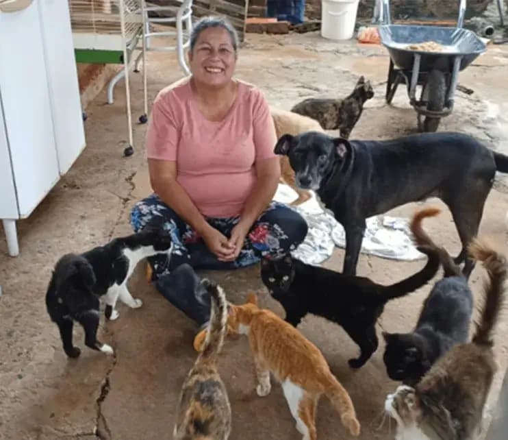 Cuidadora da Casa da Mili sentada no chão, cercada por cães e gatos acolhidos.