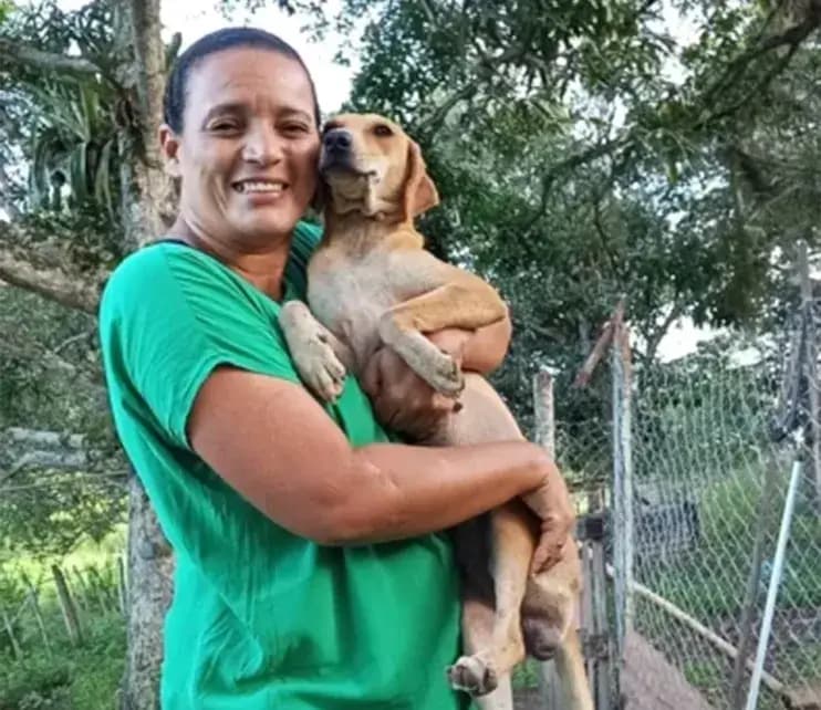 Cuidadora do Abrigo Salve Cão com um cão resgatado no colo, ao lado do cercado do abrigo em Floresta Azul.
