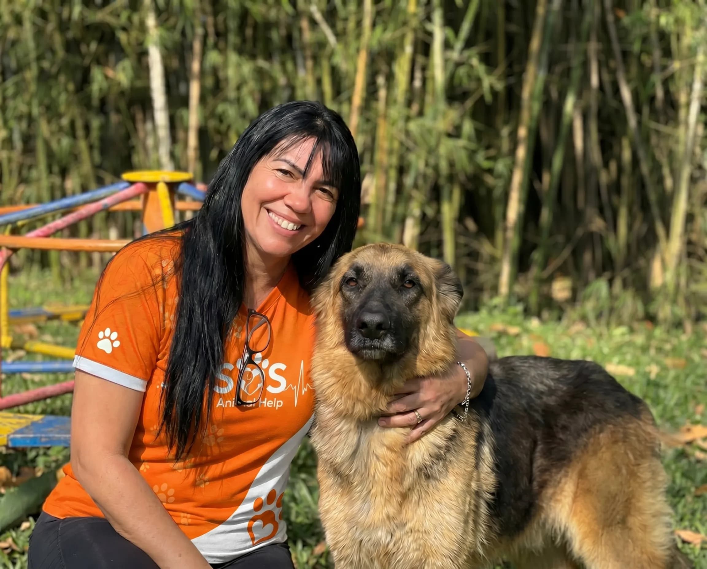Voluntária da SOS Animal Help agachada ao lado de um cão resgatado, no pátio de um dos abrigos apoiados.